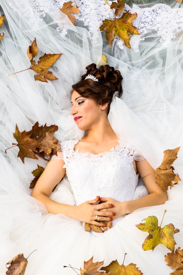 Девушка невеста в белом платье лежит с желтыми листьями