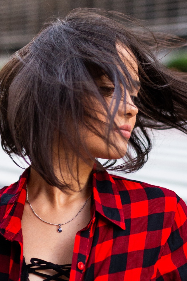 Ветер развивает волосы красивой шатенки в клетчатой рубашке