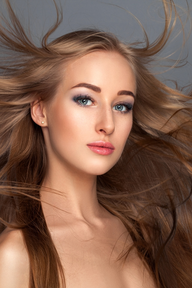 Ветер развивает волосы красивой девушке на сером фоне