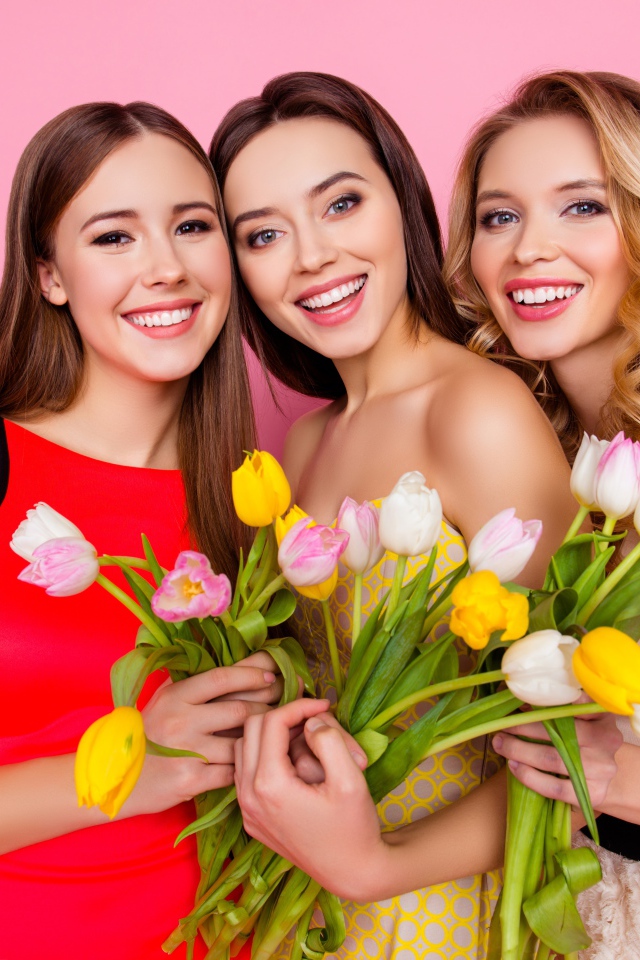 Три красивые девушки с букетами тюльпанов на розовом фоне