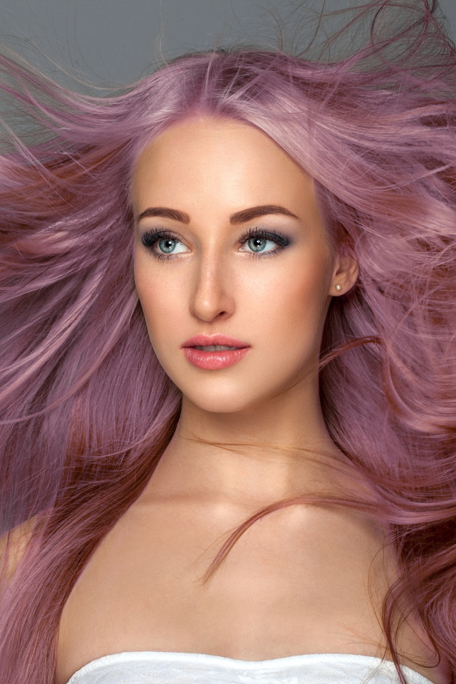 Ветер развивает розовые волосы девушки на сером фоне