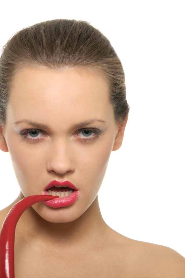 Молодая девушка кусает красный перец на белом фоне