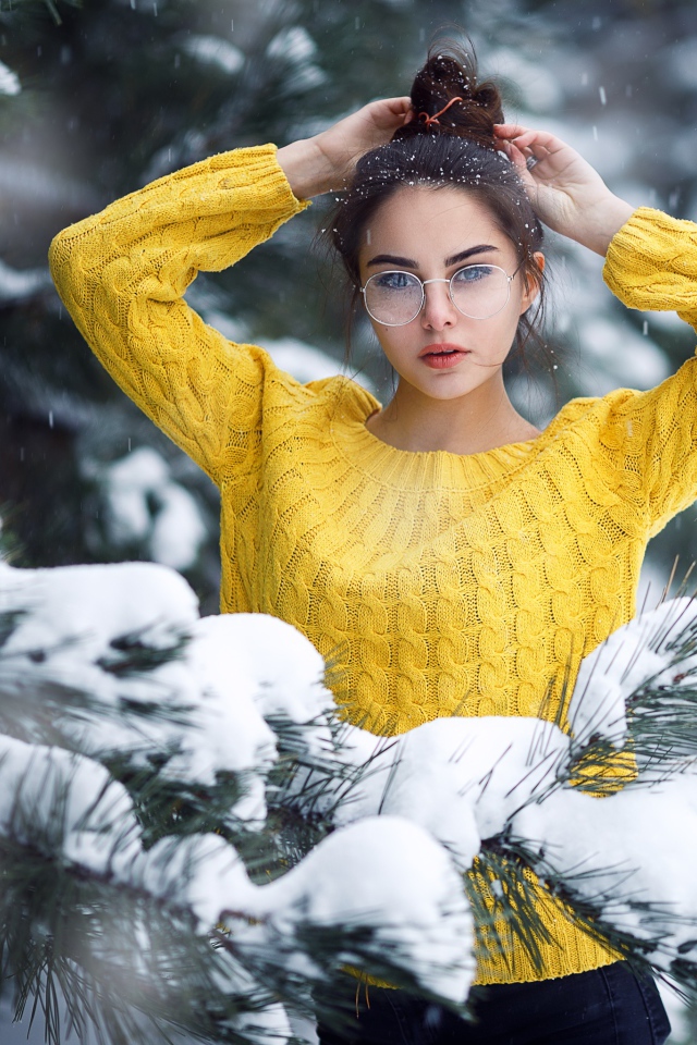 Молодая девушка в очках у заснеженной еловой ветки