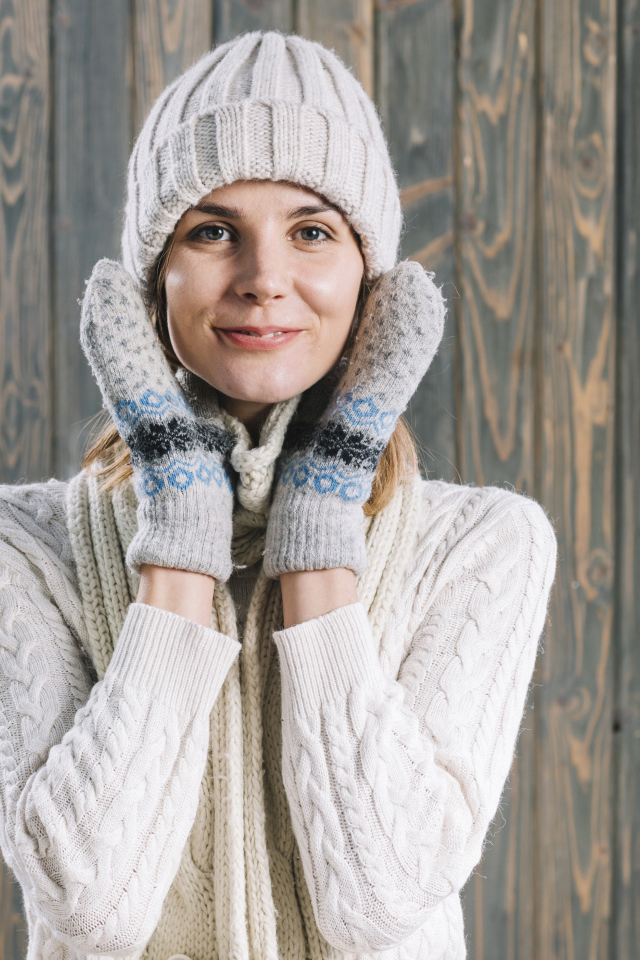 Молодая девушка на шапке, варежках  и теплой шапке на фоне забора