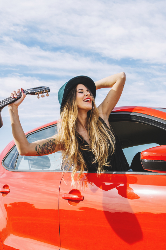 Молодая девушка с гитарой в красной машине летом