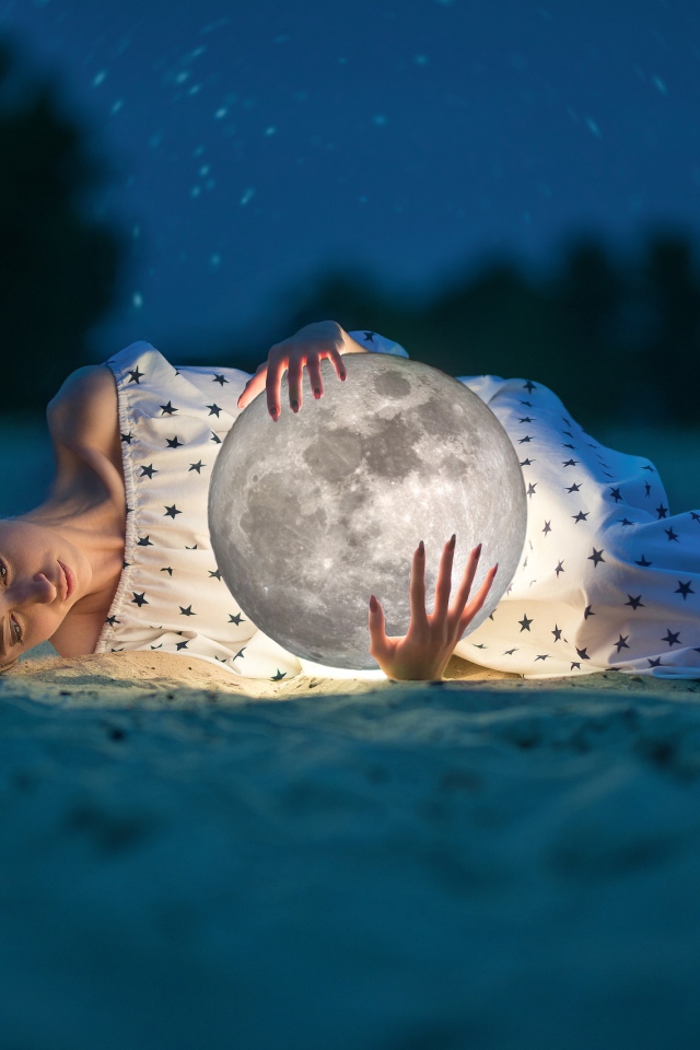 Молодая девушка с луной в руках лежит на песке