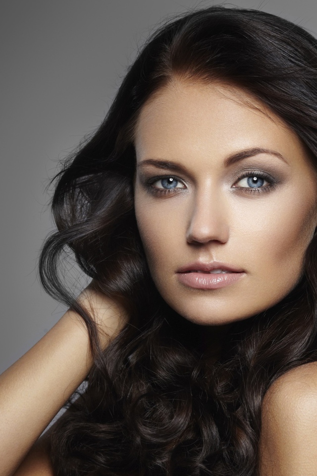 Молодая настоящая голубоглазая длинноволосая брюнетка на сером фоне