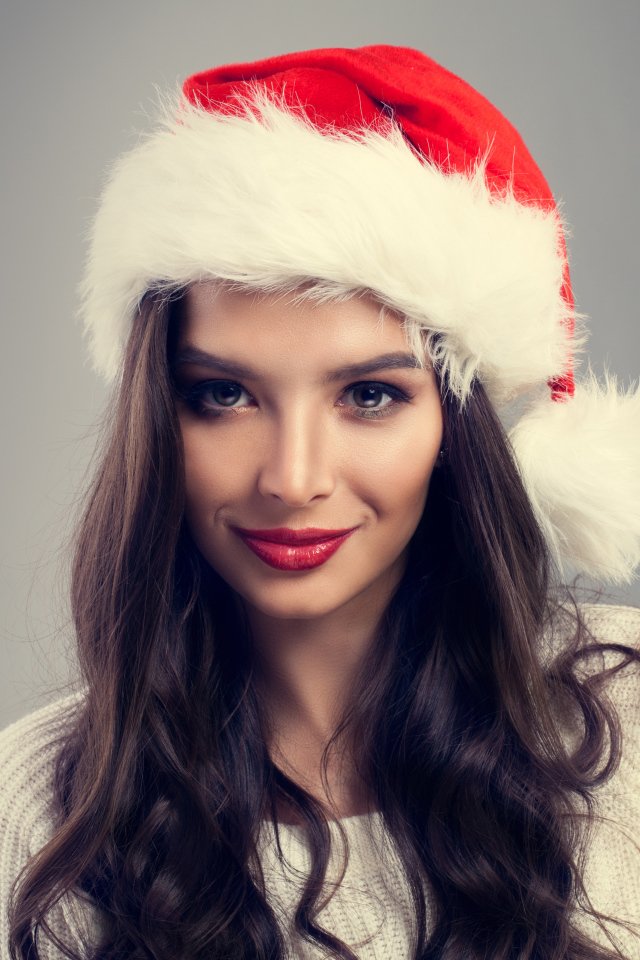 Красивая брюнетка в новогодней шапке на сером фоне