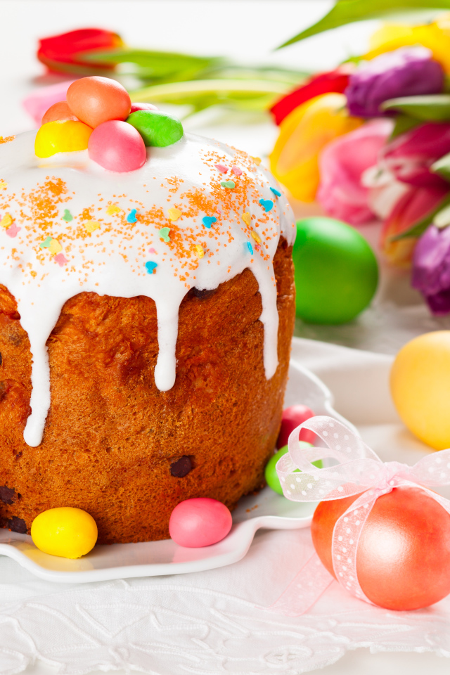 Красивый кулич с конфетами на столе с букетом тюльпанов и крашеными яйцами на Пасху