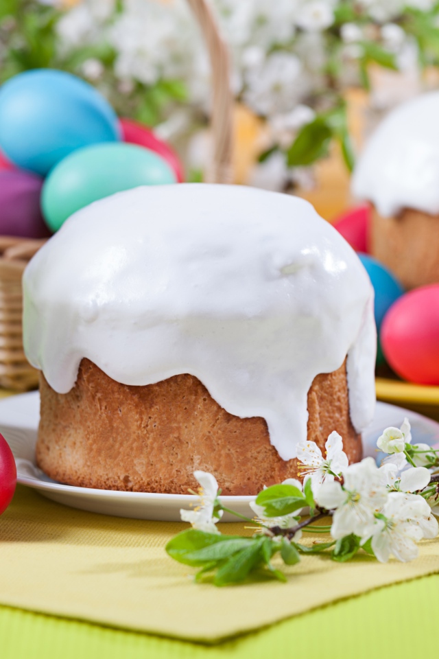 Красивый кулич с белой глазурью на столе с крашеными яйцами и веточками цветущей вишни