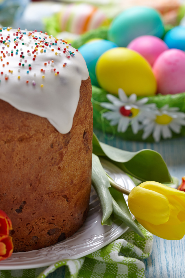 Пасхальный кулич на столе с тюльпанами и крашеными яйцами