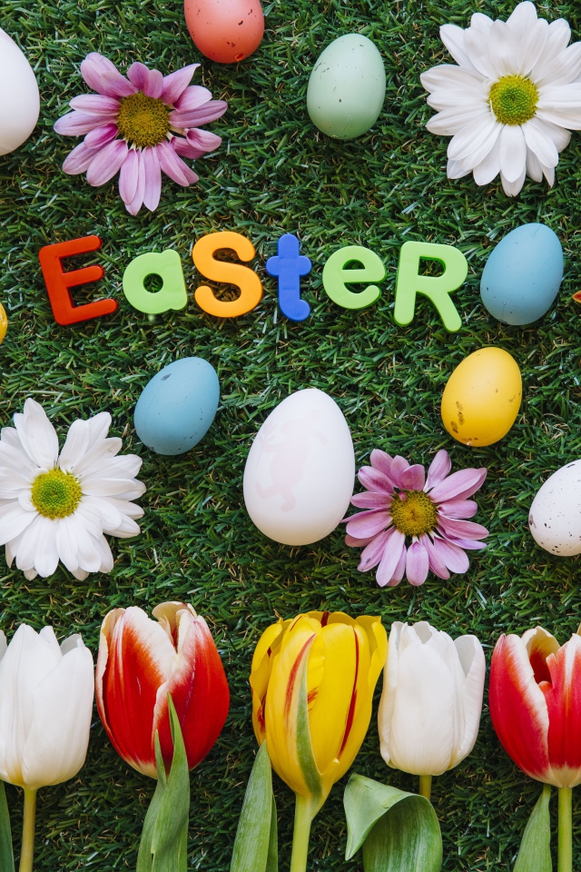 Надпись Easter на зеленой траве с крашеными яйцами и цветами
