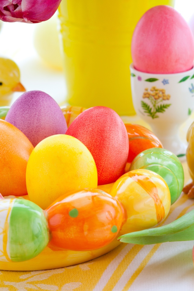 Разноцветные яйца с фигурками на столе с тюльпанами к Пасхе