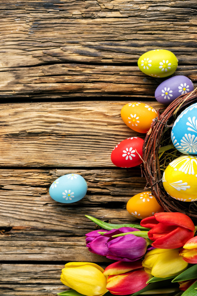 Крашеные пасхальные яйца с букетом тюльпанов на деревянном фоне
