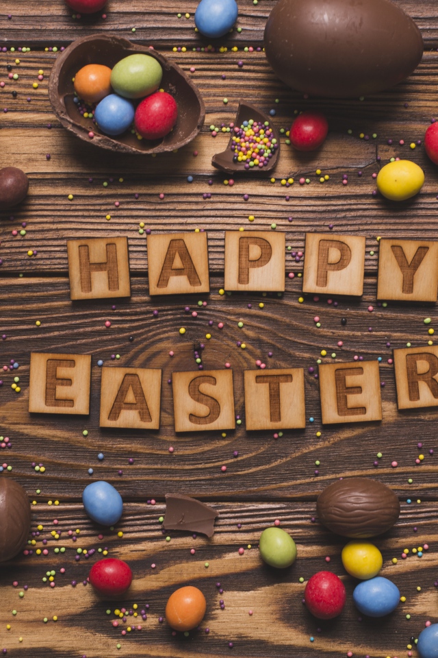 Надпись на английском Счастливой Пасхи на столе с шоколадными яйцами и конфетами