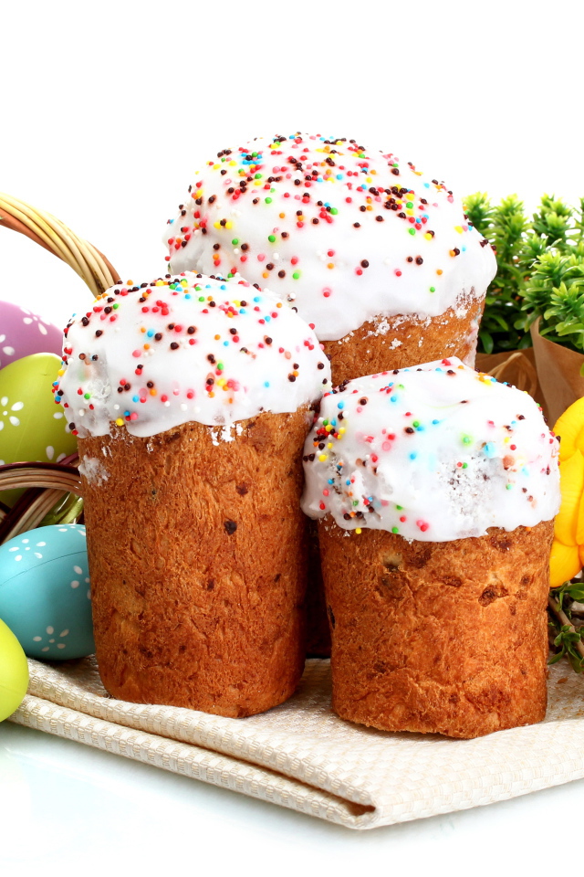 Три сладких кулича на белом фоне с цветами и крашеными яйцами к празднику Пасха