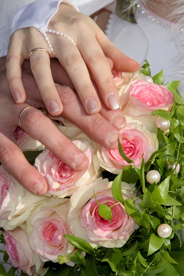 Руки жениха и невесты на букете с розовыми розами