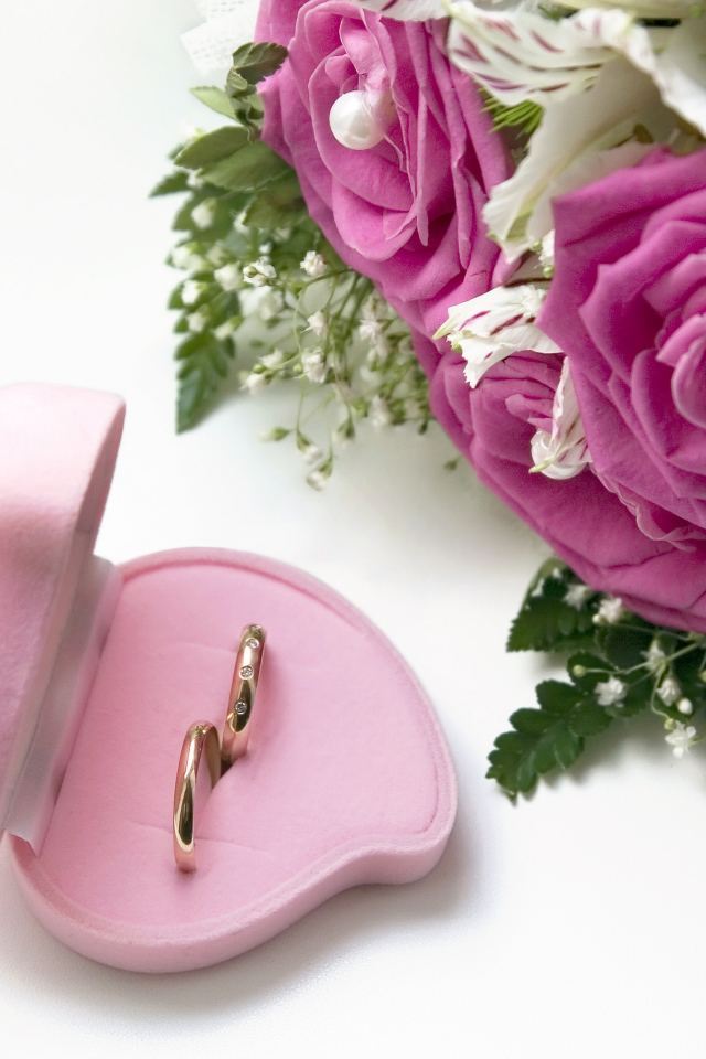 Два обручальных кольца в коробочке на белом фоне с букетом роз