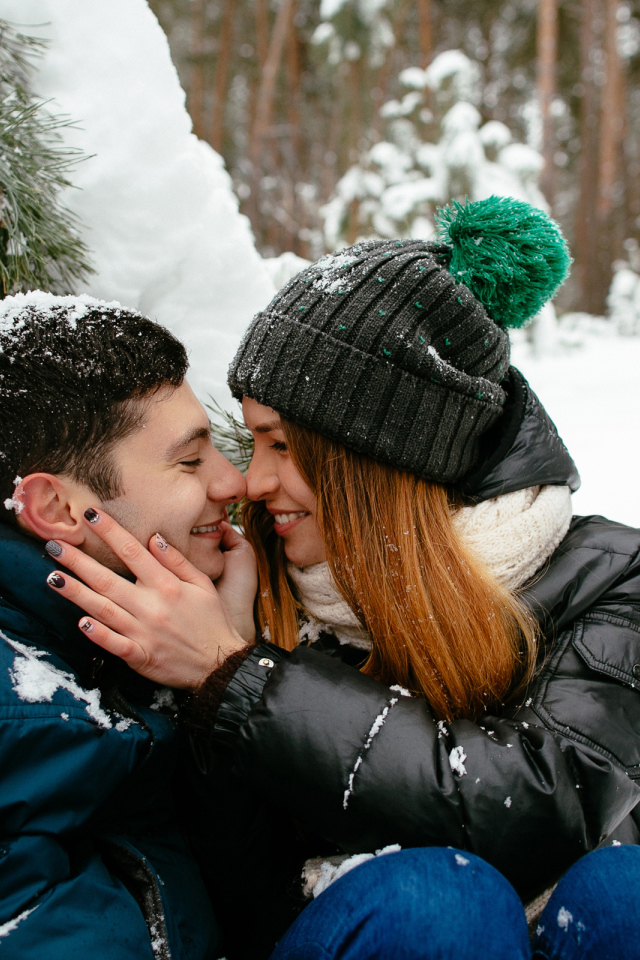 Влюбленная пара сидит под заснеженной еловой веткой зимой