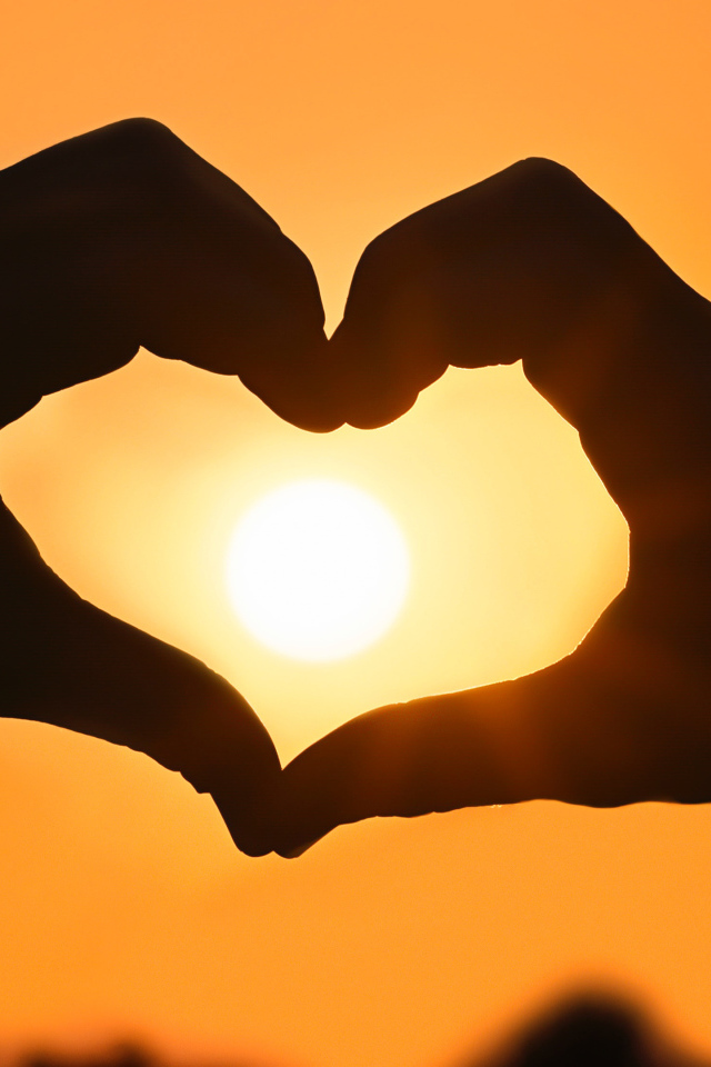 Сердце руками на фоне солнца в небе