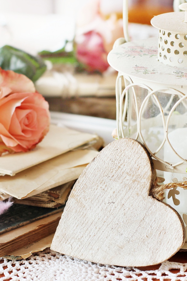 Фонарь со свечей на столе с розой, сердцем и книгами