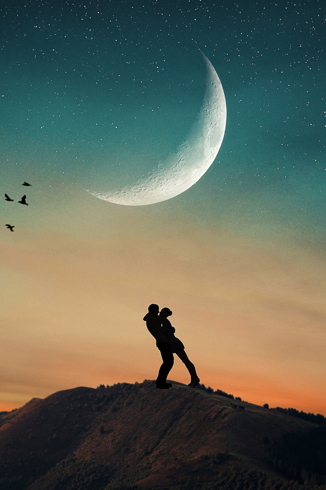 Влюбленная пара стоит на горе на фоне луны 