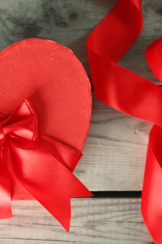 Красная коробка в форме сердца на деревянном столе с красными лентами