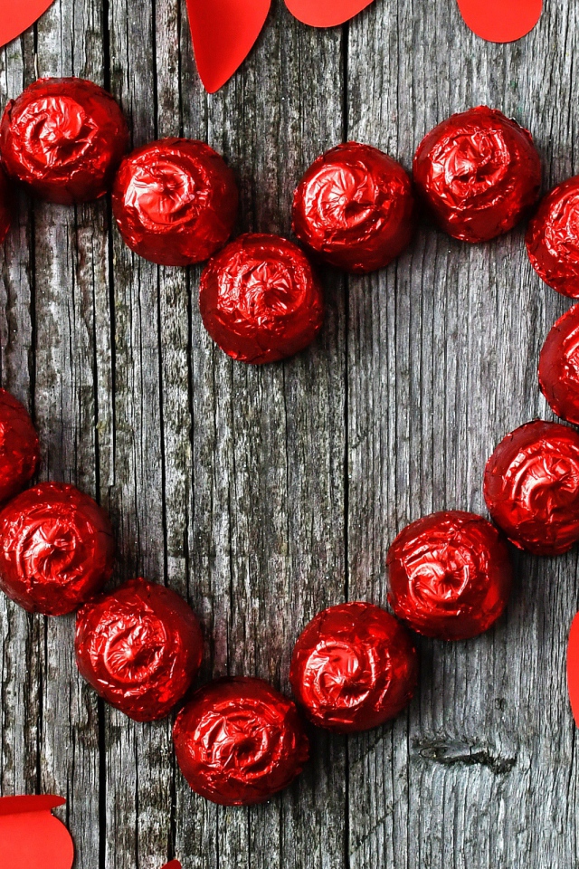 Красное сердце из конфет на деревянном фоне с бумажными сердечками