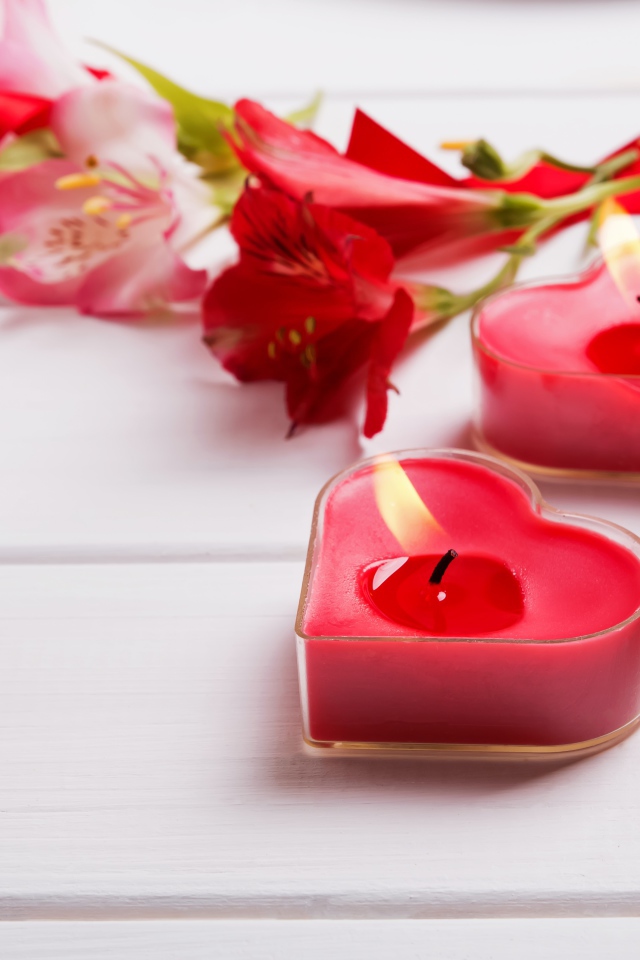 Две красные свечи в форме сердца на столе с цветами альстромерии 