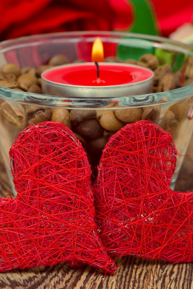 Два красных плетеных сердца на столе с зажженной свечой