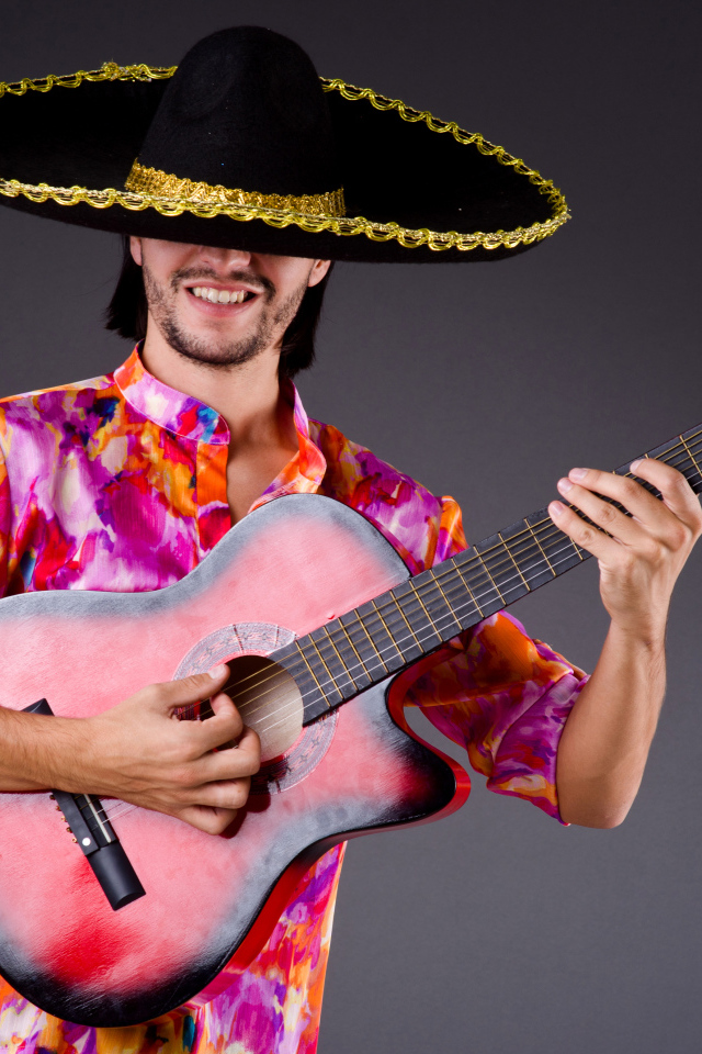 Мужчина в сомбреро с гитарой в руках на сером фоне