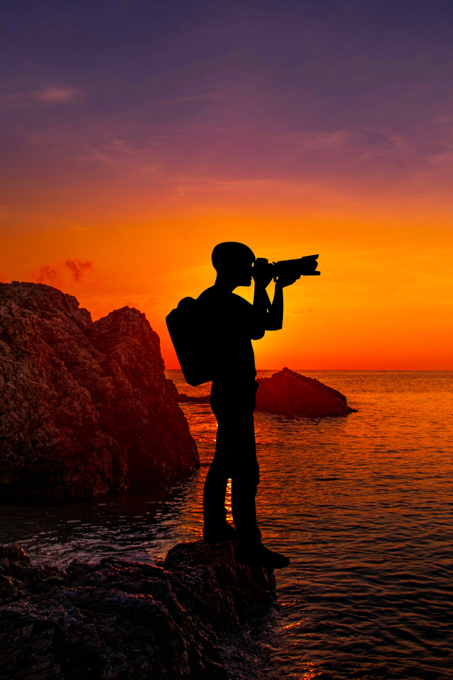 Мужчина фотографирует закат на берегу моря