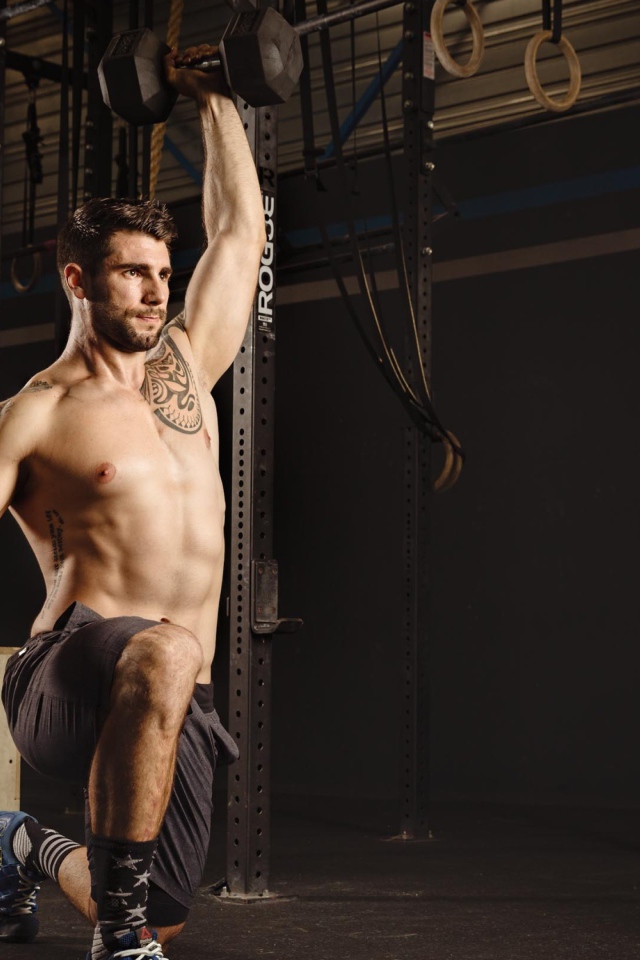 Накаченный мужчина с татуировками на теле с гантелей в руке