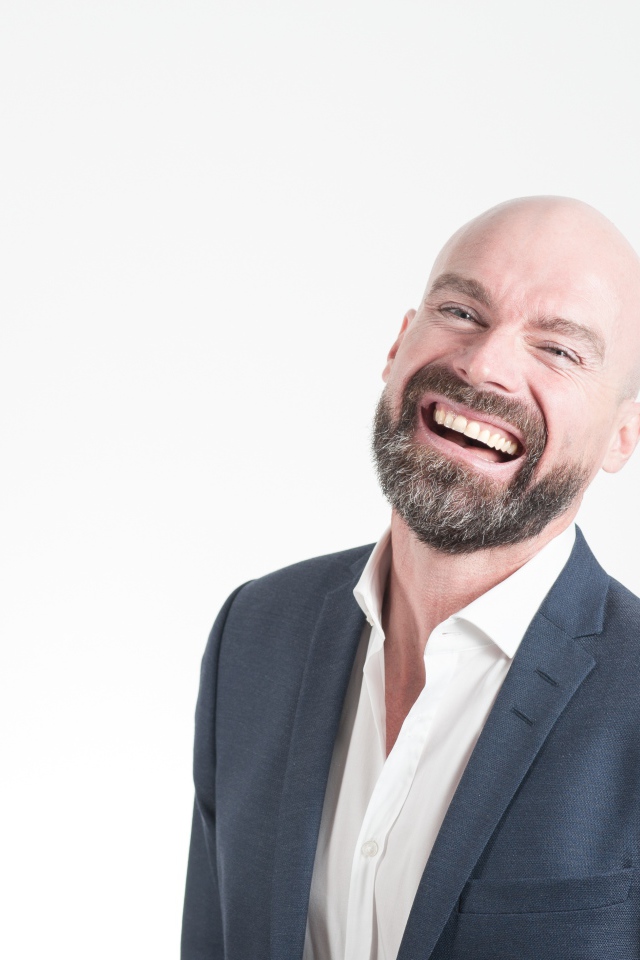 Смеющийся мужчина с бородой в костюме на сером фоне