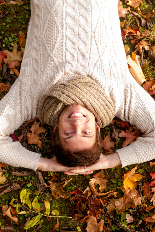 Smiling man in a sweater lies on fallen leaves