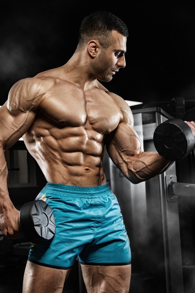 Сильный накаченный мужчина в шортах с гантелями в руках 