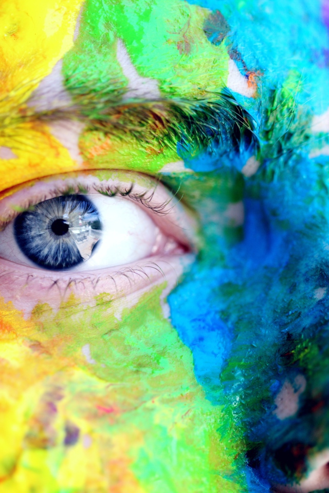 The face of a blue-eyed man in multi-colored paints close-up