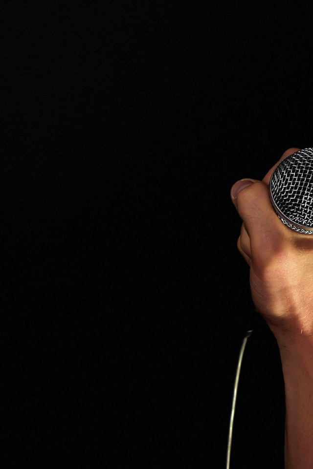 Микрофон в мужской руке на черном фоне