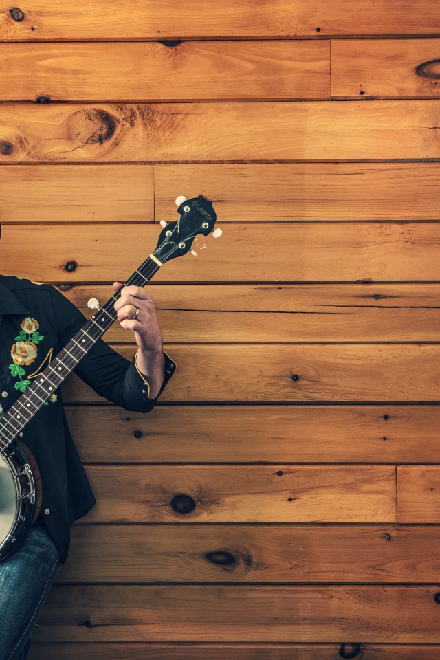 Парень музыкант играет на банджо у деревянной стены