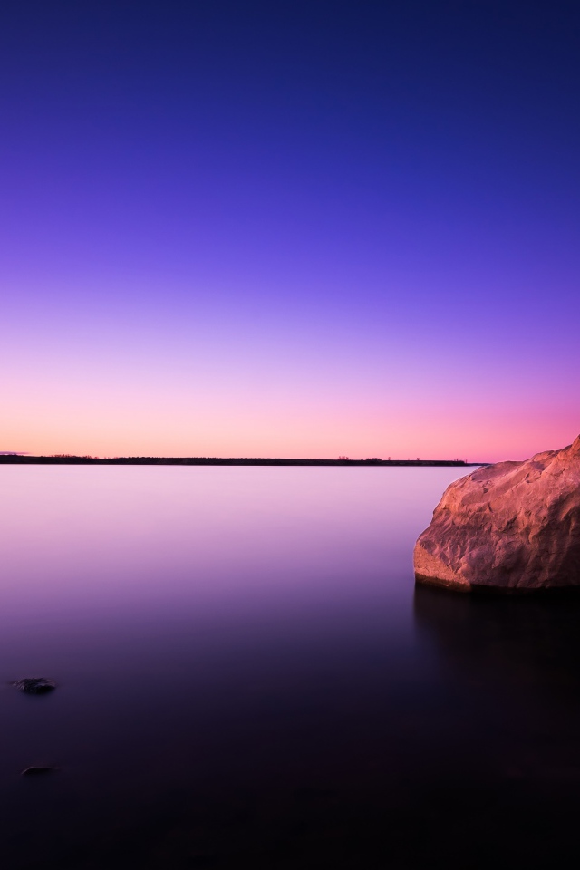 Большой камень в спокойной воде в сумерках