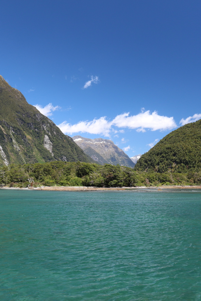 Голубая вода в озере на фоне покрытых зеленью гор под голубым небом