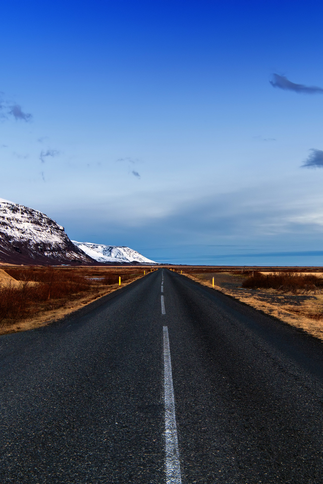 Ровная асфальтовая дорога у заснеженных гор