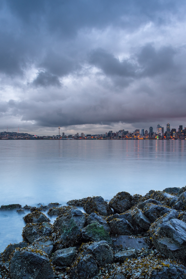 Камни на берегу реки на фоне города под пасмурным небом