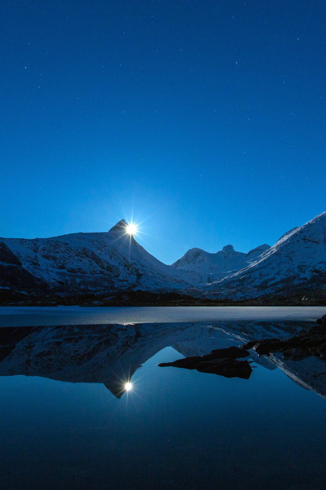 Луна и заснеженные горы отражаются в воде 