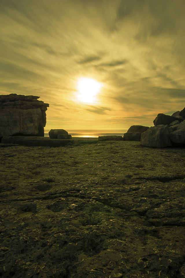 Солнце в облаках освещает камни у моря