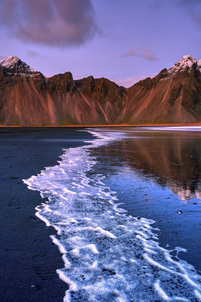 Вода на черном песке на фоне гор 