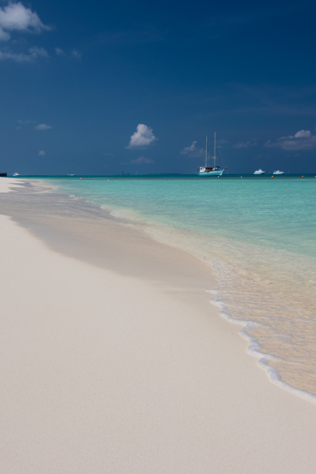 Спокойные волны на белом горячем песке под голубым небом
