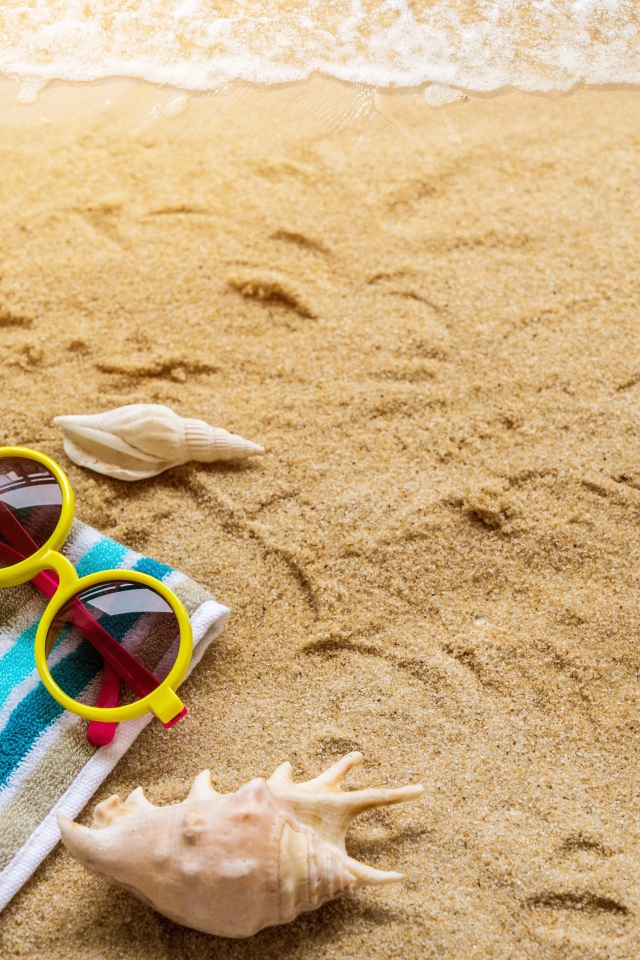 Шляпа, очки, полотенце и ракушки на желтом песке у моря