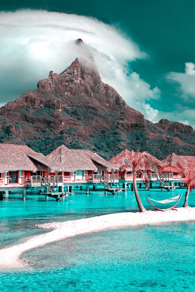 Дома на сваях в голубом океане на фоне горы под белыми облаками