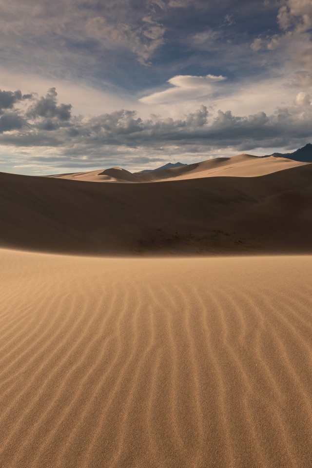 Волнистый песок под небом с белыми облаками
